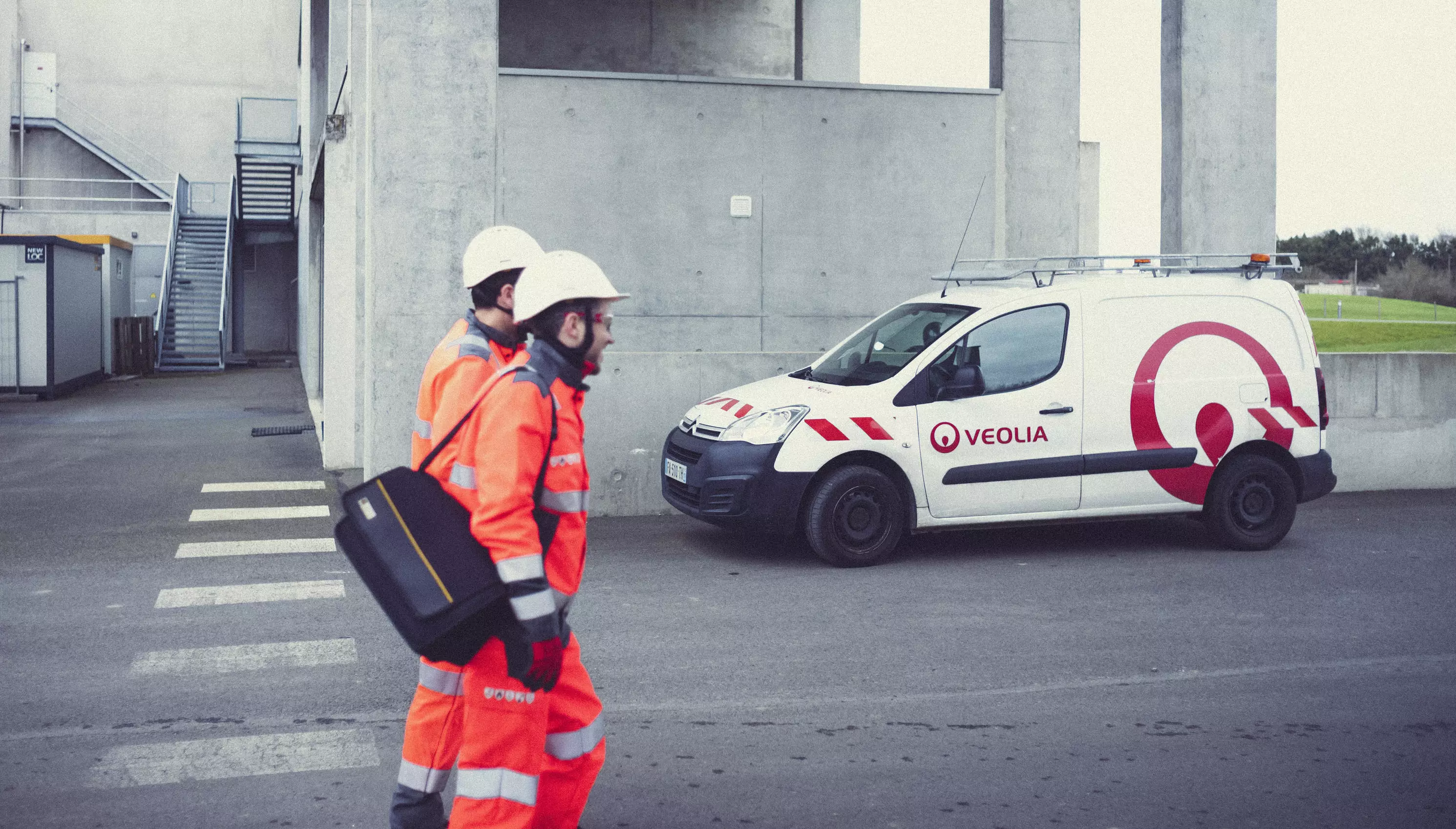 Deux techniciens Veolia en équipements marchent chez un client pour effectuer un service industriel devant un camion Veolia