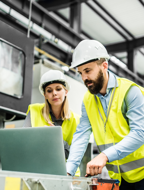 Deux personnes avec un gilet réfléchissant et un casque travaillent sur un projet sur un ordinateur dans un site industriel